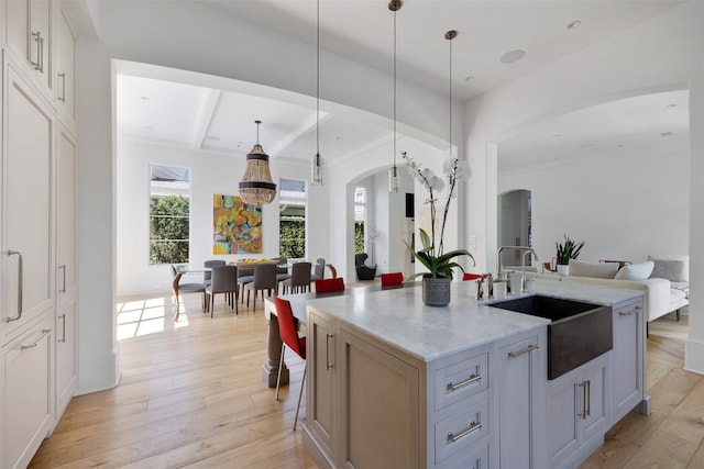 kitchen with sink, hanging light fixtures, light hardwood / wood-style floors, a center island with sink, and white cabinets