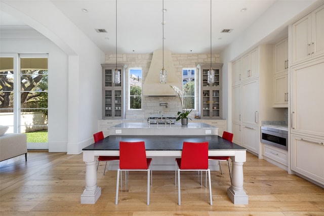 kitchen with a kitchen bar, stainless steel microwave, decorative light fixtures, and light wood-type flooring