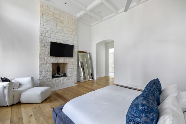 bedroom with a high ceiling, coffered ceiling, beamed ceiling, a fireplace, and hardwood / wood-style flooring