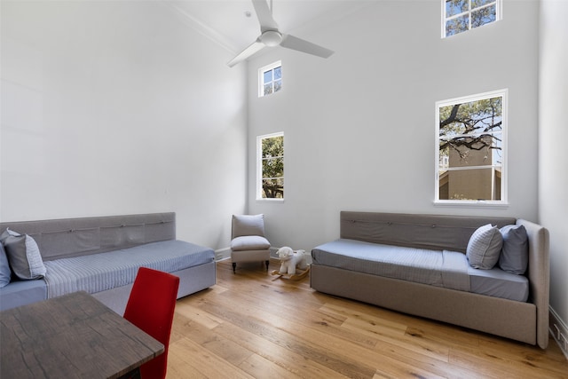 living room featuring ceiling fan, light hardwood / wood-style floors, ornamental molding, and a high ceiling