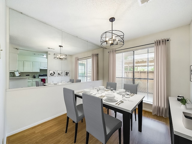 dining space featuring wood-type flooring, a textured ceiling, and an inviting chandelier