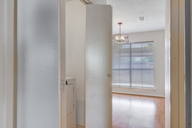 hallway featuring washer / clothes dryer, light hardwood / wood-style flooring, a textured ceiling, and a notable chandelier