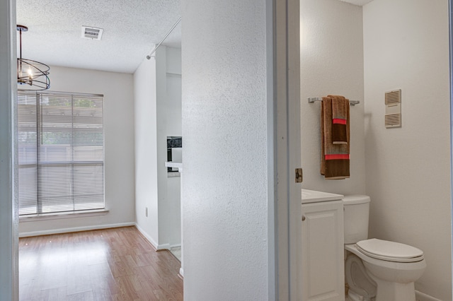 bathroom with a textured ceiling, hardwood / wood-style flooring, toilet, and a notable chandelier