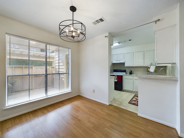 kitchen featuring black range with electric cooktop, pendant lighting, light hardwood / wood-style flooring, a notable chandelier, and white cabinetry