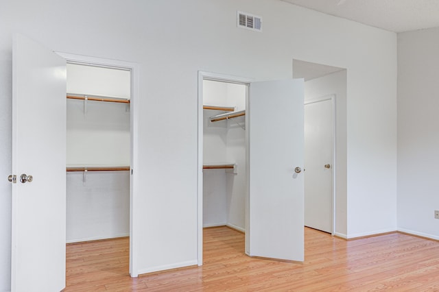 unfurnished bedroom featuring multiple closets and light wood-type flooring