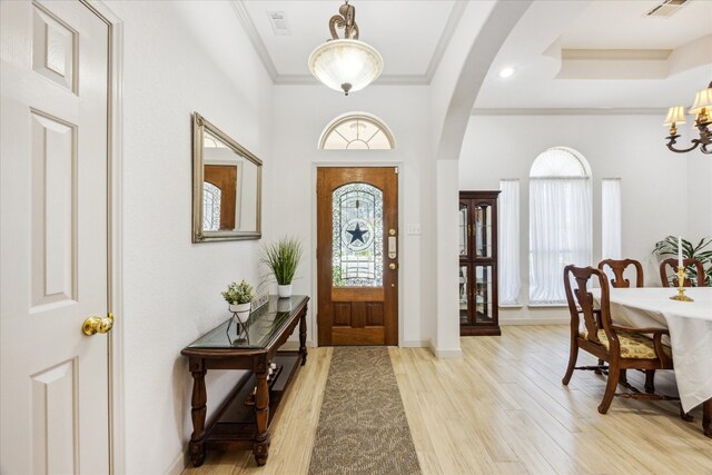 foyer with crown molding, light hardwood / wood-style floors, and a notable chandelier