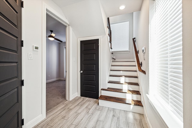 staircase featuring ceiling fan, a healthy amount of sunlight, wood-type flooring, and lofted ceiling