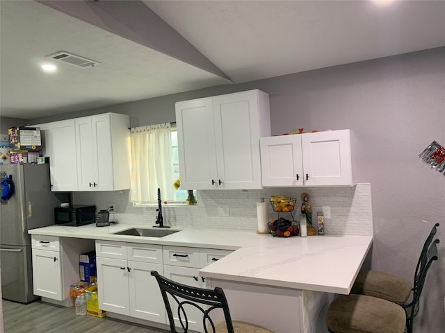 kitchen with backsplash, sink, light wood-type flooring, white cabinetry, and a breakfast bar area