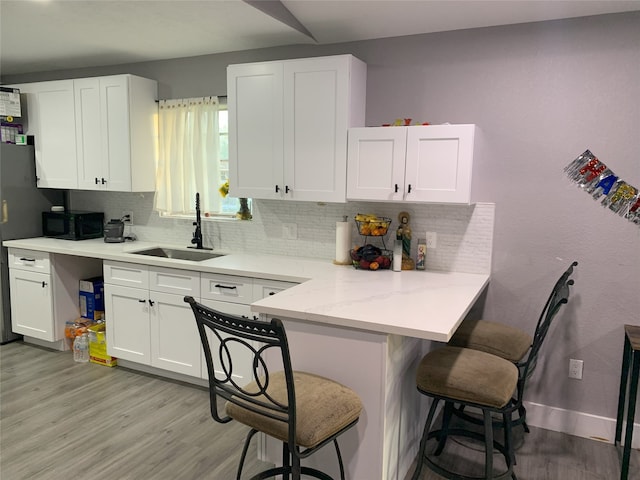 kitchen with white cabinetry, sink, light hardwood / wood-style floors, a kitchen bar, and decorative backsplash