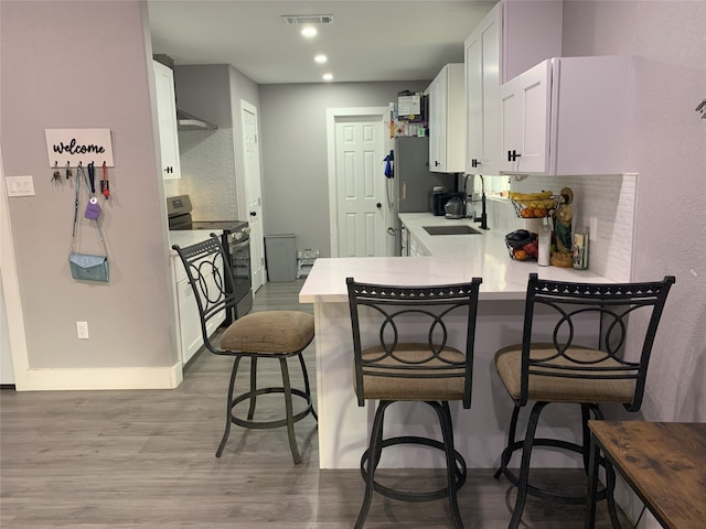 kitchen featuring sink, light wood-type flooring, black / electric stove, a kitchen bar, and kitchen peninsula