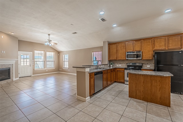 kitchen with a tile fireplace, ceiling fan, stainless steel appliances, kitchen peninsula, and vaulted ceiling