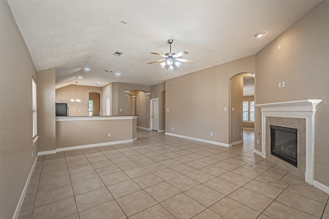 unfurnished living room with ceiling fan, vaulted ceiling, light tile patterned floors, and a tiled fireplace