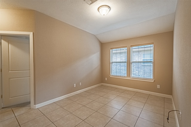 tiled empty room featuring a textured ceiling and lofted ceiling