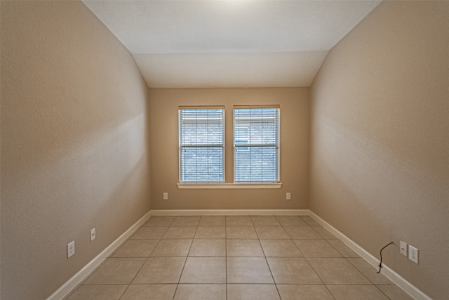 tiled empty room featuring lofted ceiling