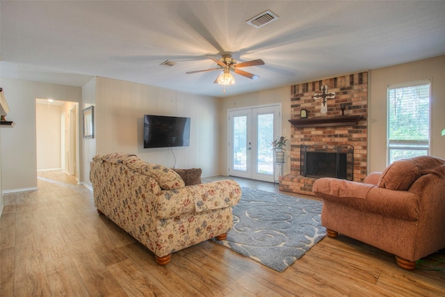 living room with french doors, a wealth of natural light, a brick fireplace, and light wood-type flooring