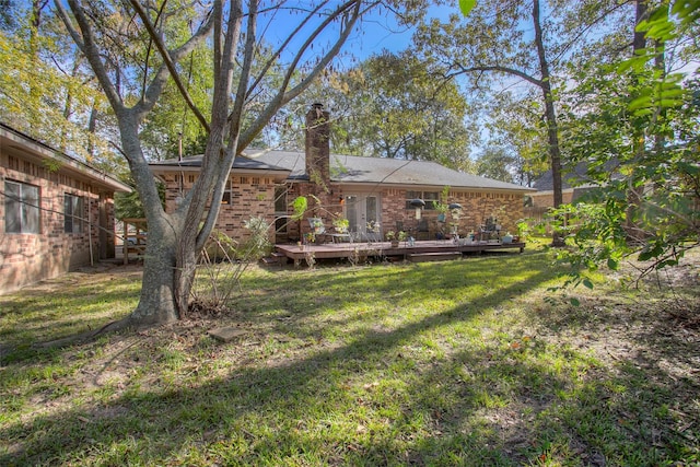 back of property with brick siding, a lawn, a chimney, and a wooden deck