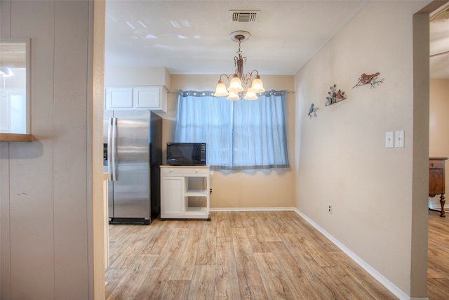 kitchen with white cabinets, stainless steel fridge, light wood-type flooring, and hanging light fixtures