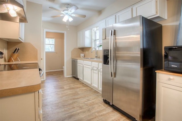 kitchen featuring sink, wall chimney exhaust hood, light hardwood / wood-style floors, white cabinets, and appliances with stainless steel finishes