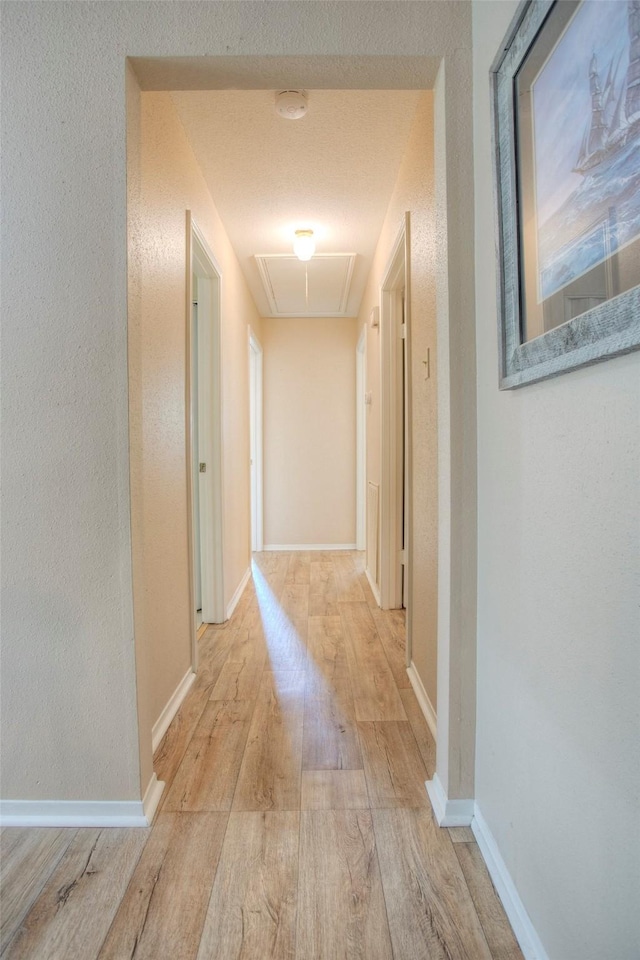 corridor with light wood-type flooring, attic access, and baseboards