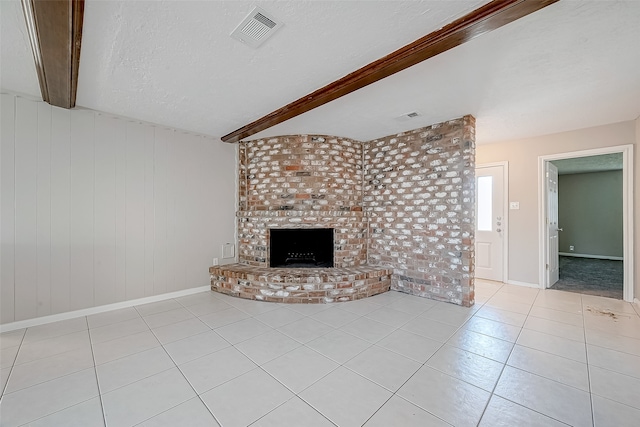 unfurnished living room featuring light tile patterned flooring, a brick fireplace, a textured ceiling, beamed ceiling, and wood walls