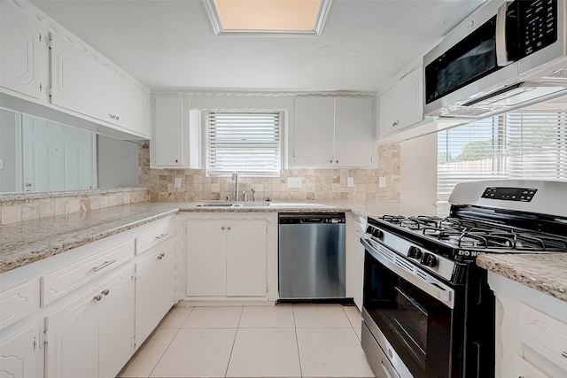 kitchen with sink, stainless steel appliances, light tile patterned floors, backsplash, and white cabinets