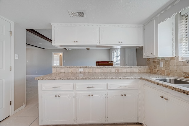 kitchen with kitchen peninsula, tasteful backsplash, a textured ceiling, light tile patterned floors, and white cabinetry