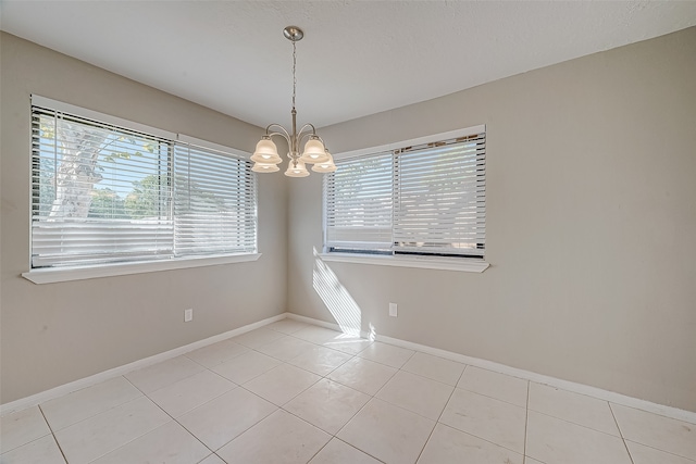 tiled spare room featuring a chandelier and a wealth of natural light