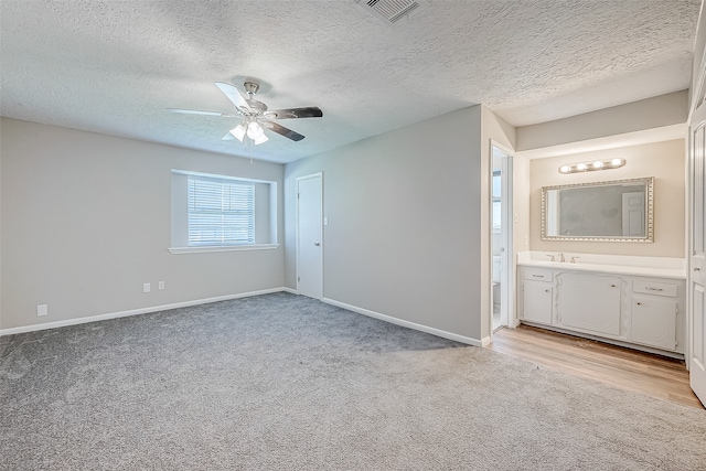 unfurnished bedroom with a textured ceiling, light colored carpet, ensuite bath, and ceiling fan