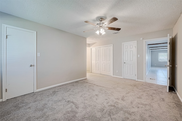 unfurnished bedroom featuring light carpet, a textured ceiling, two closets, and ceiling fan