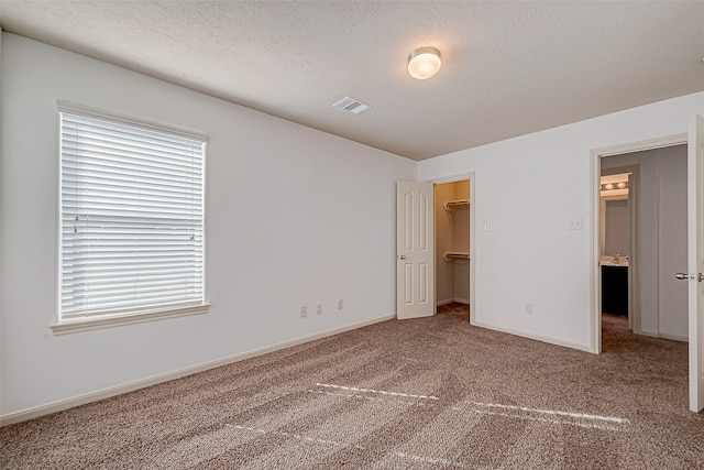 unfurnished bedroom with carpet flooring, a walk in closet, a textured ceiling, and a closet