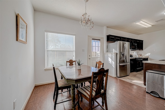 dining area with a textured ceiling, light hardwood / wood-style flooring, and a notable chandelier