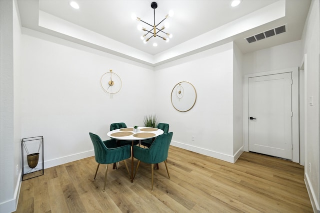 dining space featuring a raised ceiling, an inviting chandelier, and light wood-type flooring