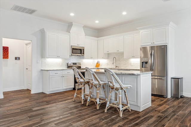 kitchen featuring appliances with stainless steel finishes, dark hardwood / wood-style flooring, light stone counters, crown molding, and white cabinetry