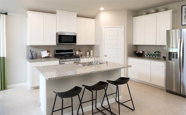 kitchen featuring backsplash, a kitchen island with sink, white cabinets, and stainless steel appliances