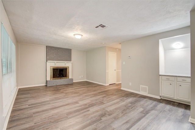 unfurnished living room featuring a textured ceiling, light hardwood / wood-style floors, and a brick fireplace