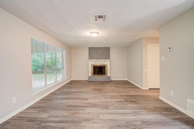 unfurnished living room with light hardwood / wood-style floors, a textured ceiling, and a brick fireplace