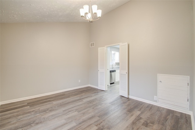 unfurnished room with sink, an inviting chandelier, high vaulted ceiling, wood-type flooring, and a textured ceiling