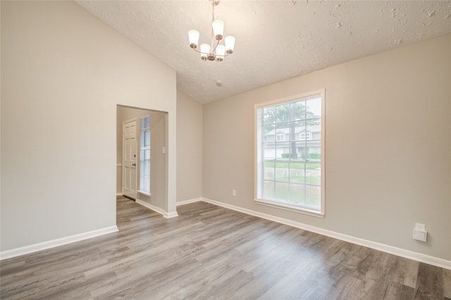 unfurnished room featuring light hardwood / wood-style floors, an inviting chandelier, a textured ceiling, and vaulted ceiling