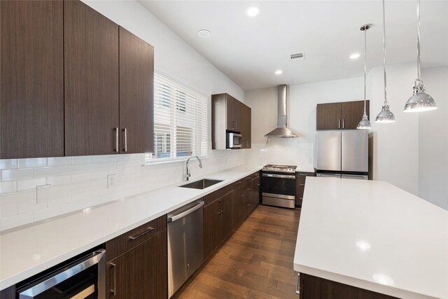 kitchen with sink, wall chimney exhaust hood, wine cooler, decorative light fixtures, and appliances with stainless steel finishes