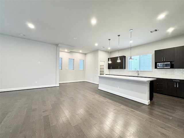 kitchen featuring visible vents, light countertops, tasteful backsplash, stainless steel microwave, and dark wood finished floors