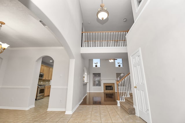 tiled foyer with ceiling fan, a towering ceiling, and crown molding