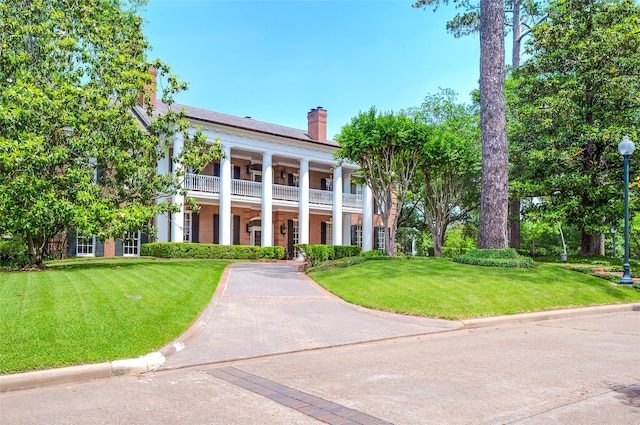 greek revival house featuring a balcony and a front lawn