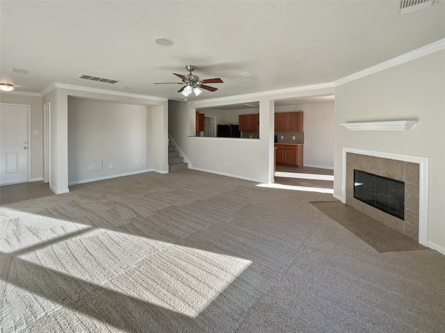 unfurnished living room featuring ceiling fan, light colored carpet, ornamental molding, and a fireplace