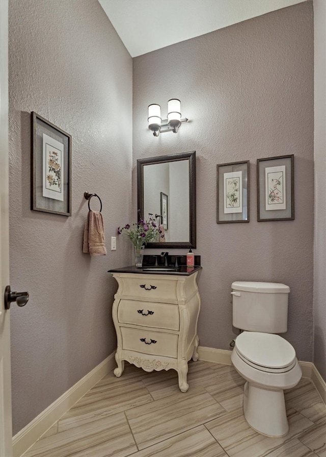 half bath with toilet, baseboards, and vanity