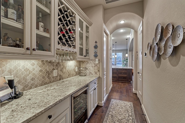 bar with wine cooler, decorative backsplash, light stone countertops, dark hardwood / wood-style flooring, and white cabinetry