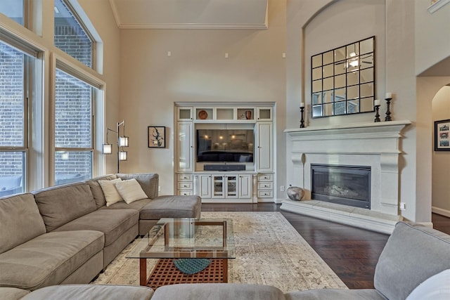 living area with wood finished floors, a towering ceiling, baseboards, a glass covered fireplace, and crown molding