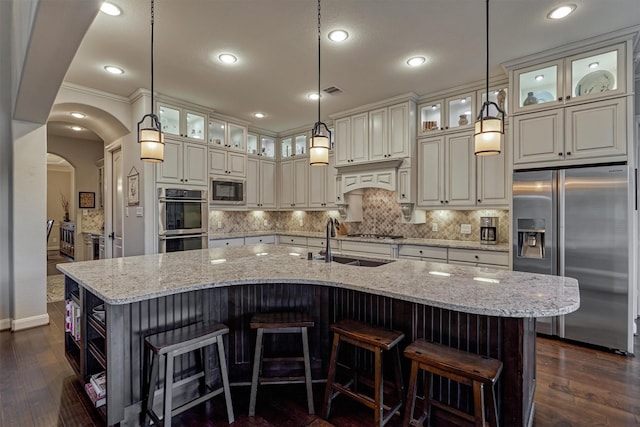 kitchen featuring arched walkways, decorative backsplash, a large island, appliances with stainless steel finishes, and a sink