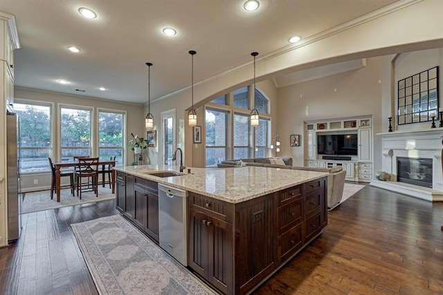 kitchen with stainless steel appliances, ornamental molding, open floor plan, a sink, and dark brown cabinetry