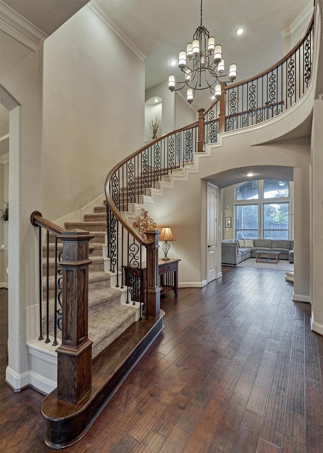 stairs with arched walkways, crown molding, wood-type flooring, a towering ceiling, and baseboards