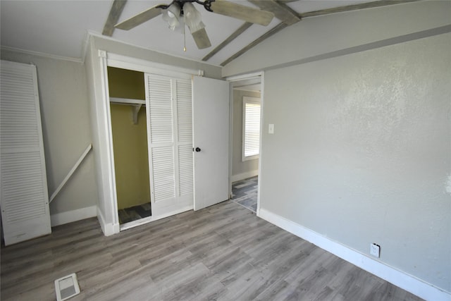 unfurnished bedroom featuring hardwood / wood-style flooring, vaulted ceiling with beams, ceiling fan, ornamental molding, and a closet